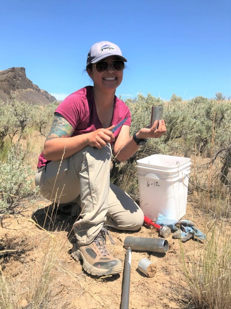 a person in a field with a bucket and soil sample.