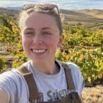 A woman in overalls taking a selfie in a vineyard.