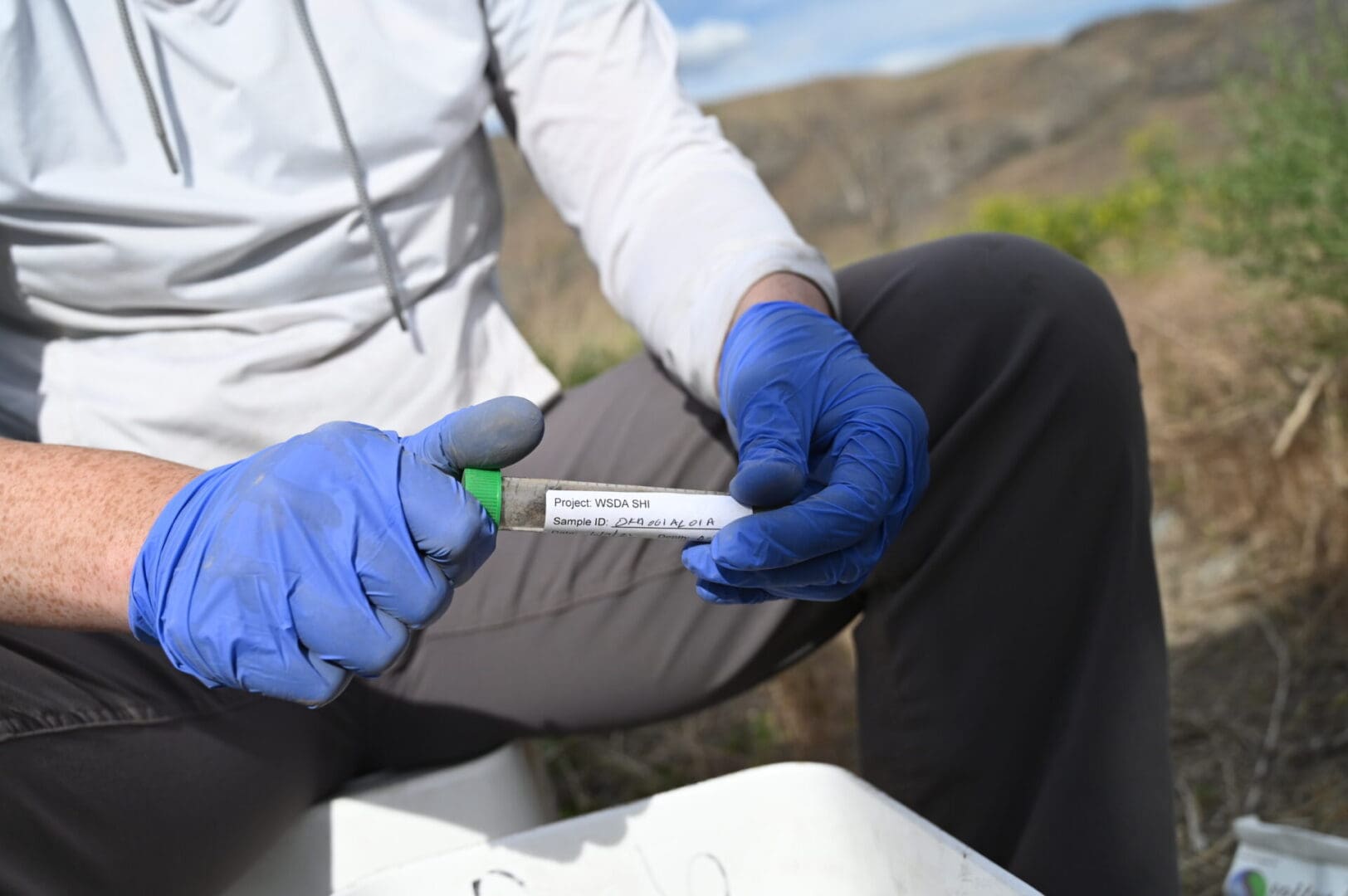 a person holding a labeled test tube in a field.