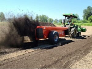 a tractor pulling a compost spreader through a field.