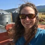 A woman in sunglasses is taking a selfie in front of a grain silo in the picturesque pasture.