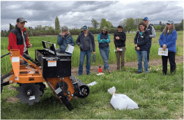 A group of people standing in a field with a tractor.