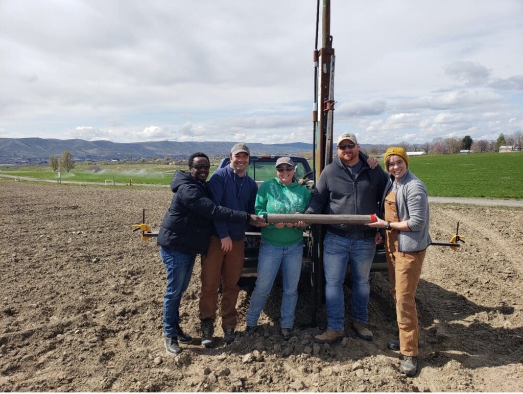 Four people standing next to a tractor in a field.