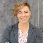 A smiling woman in a gray blazer and floral shirt, passionately discussing soil health.