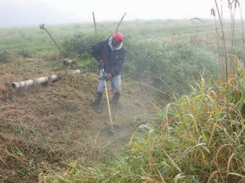 A man in a red cap using a weed trimmer in a grassy field on a foggy day.