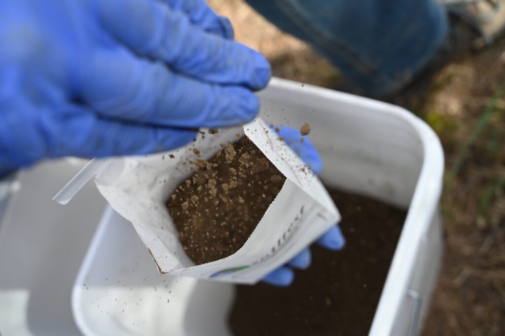 a gloved hand putting soil into a bag.