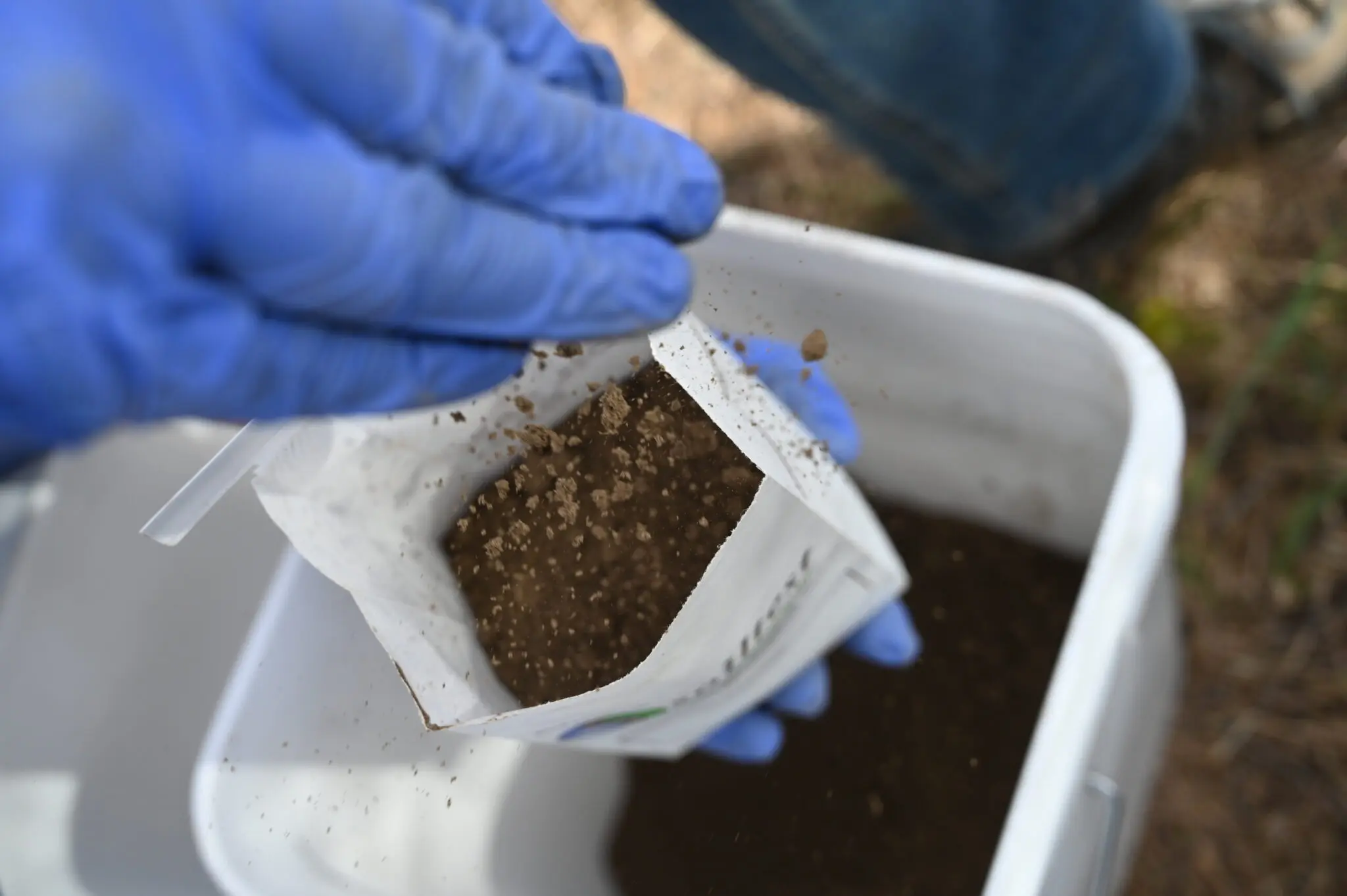 a gloved hand putting soil into a bag.