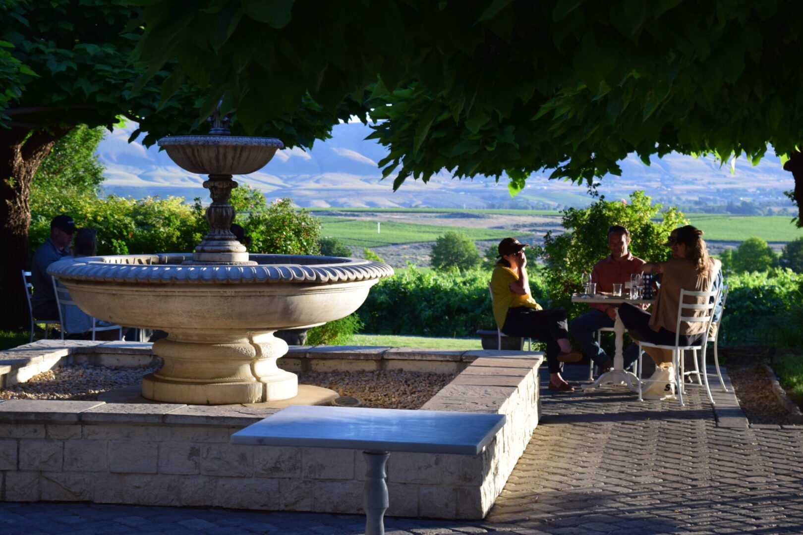 a fountain on a brick patio with people having a conversation in the background.