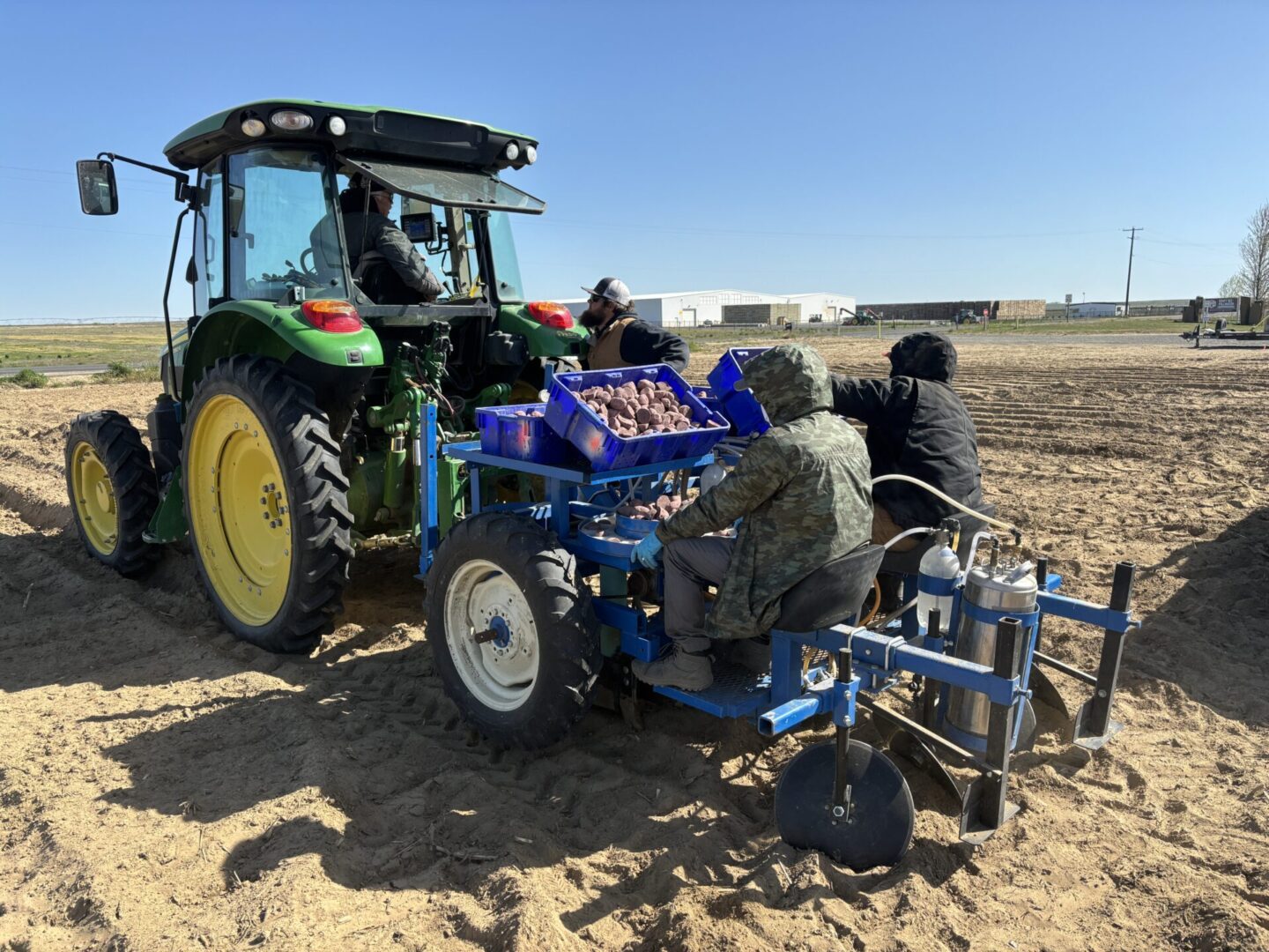 two people riding behind a tractor planting potatoes.