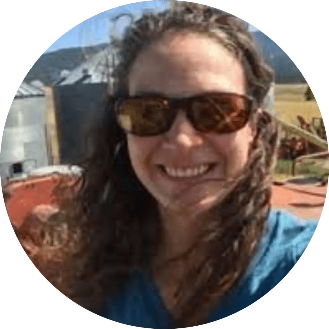 Photo of a woman wearing sunglasses standing in front of a farm landscape.